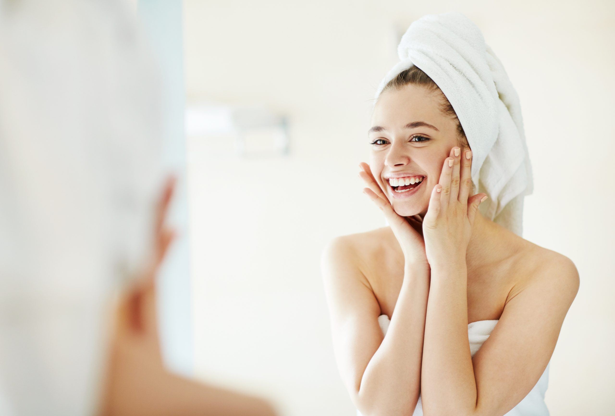 Happy girl looking at her face in mirror after bath